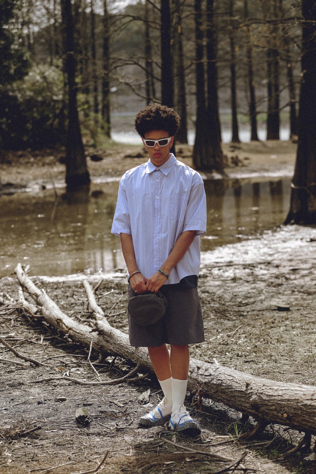 Model wearing a pale blue pinstriped short-sleeve button-up shirt with dark shorts outdoors.