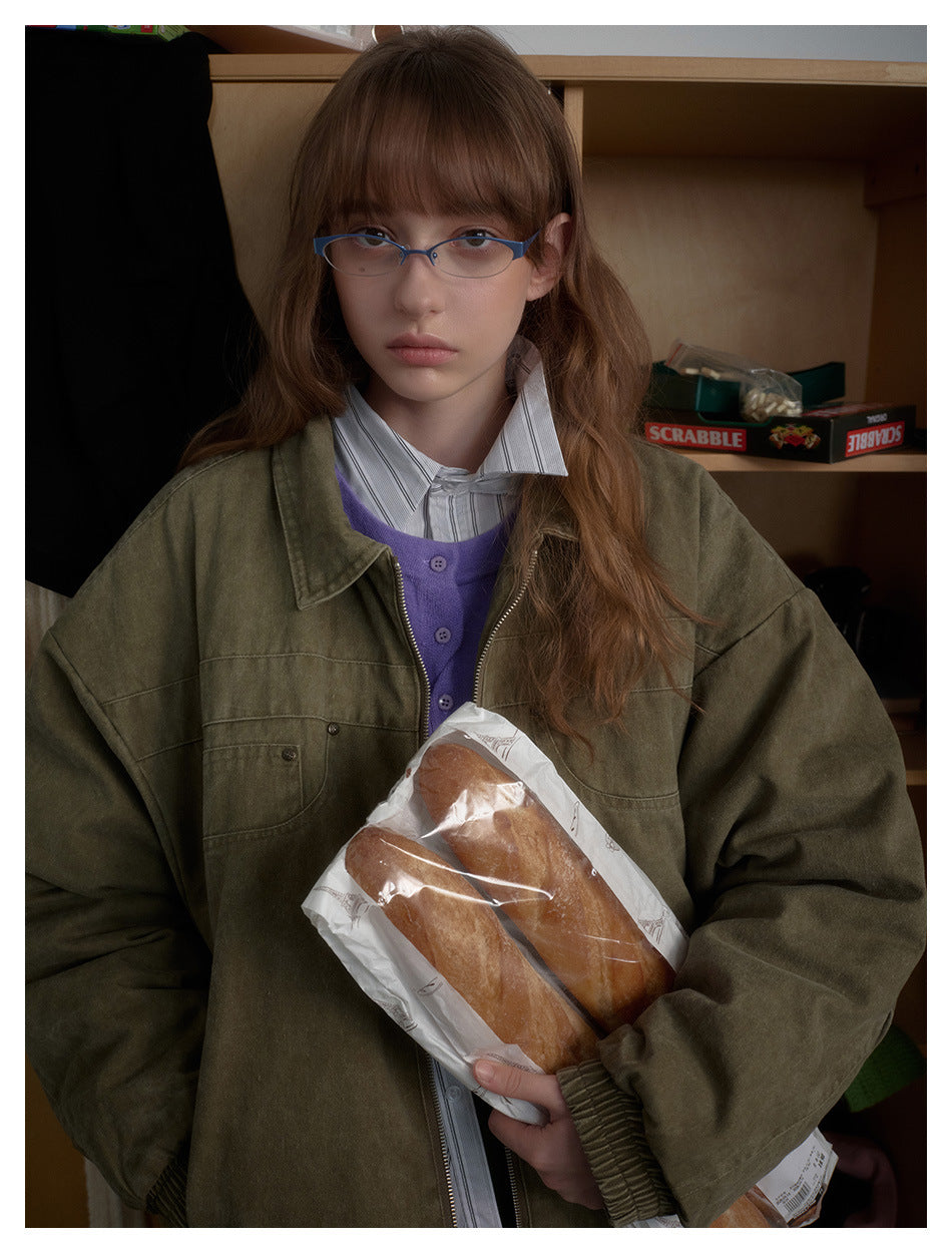 Front view of a model in an oversized olive jacket with a wide collar and chest pockets, holding a bag of bread.