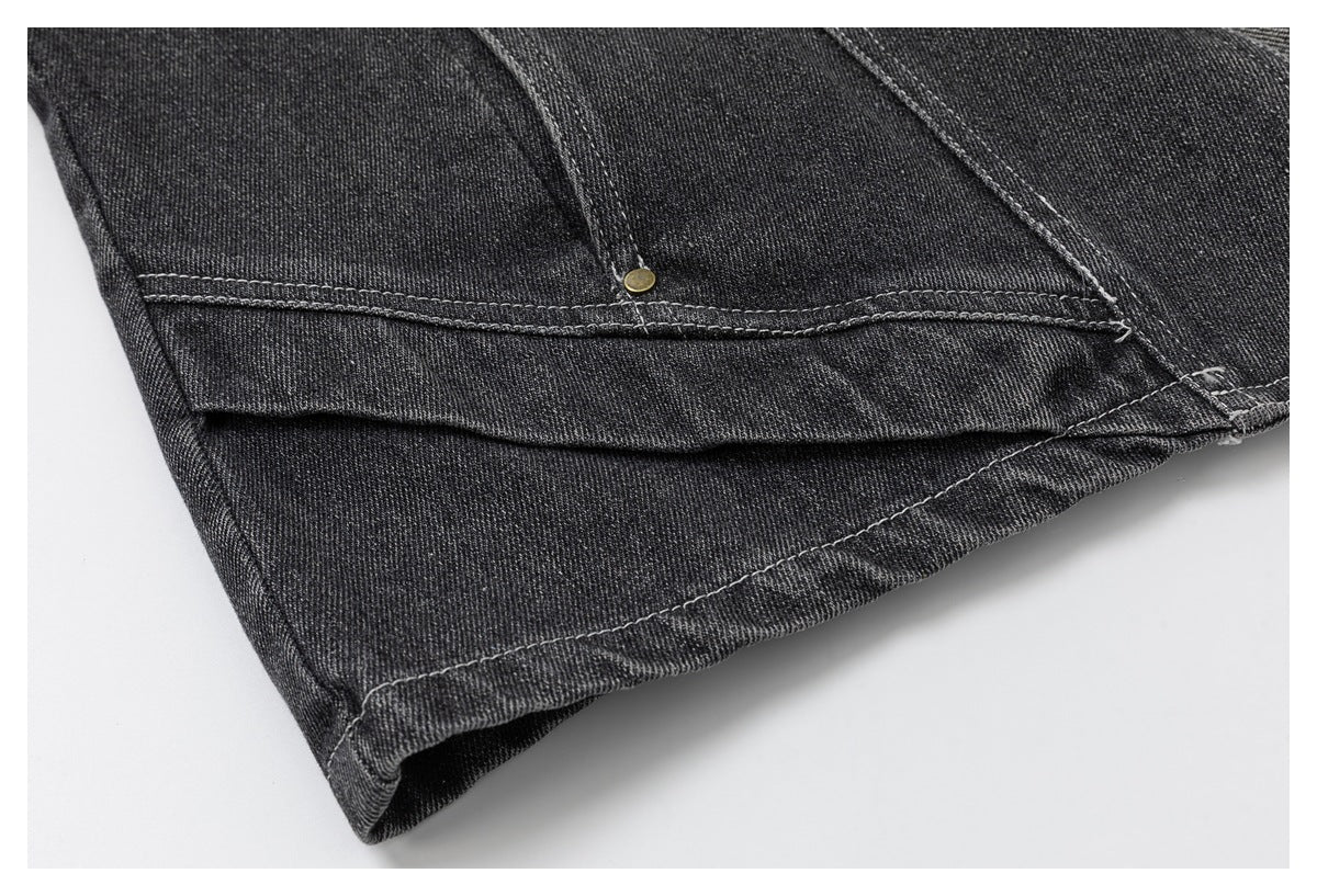 Close-up of a charcoal denim garment hem showing layered seams and a small brass-tone rivet.