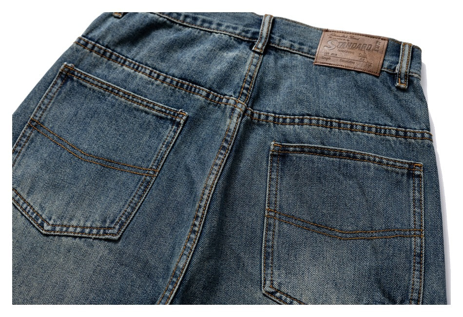 Close-up of blue faded jeans from the back, showing two stitched pockets, belt loops and a brown waistband patch.
