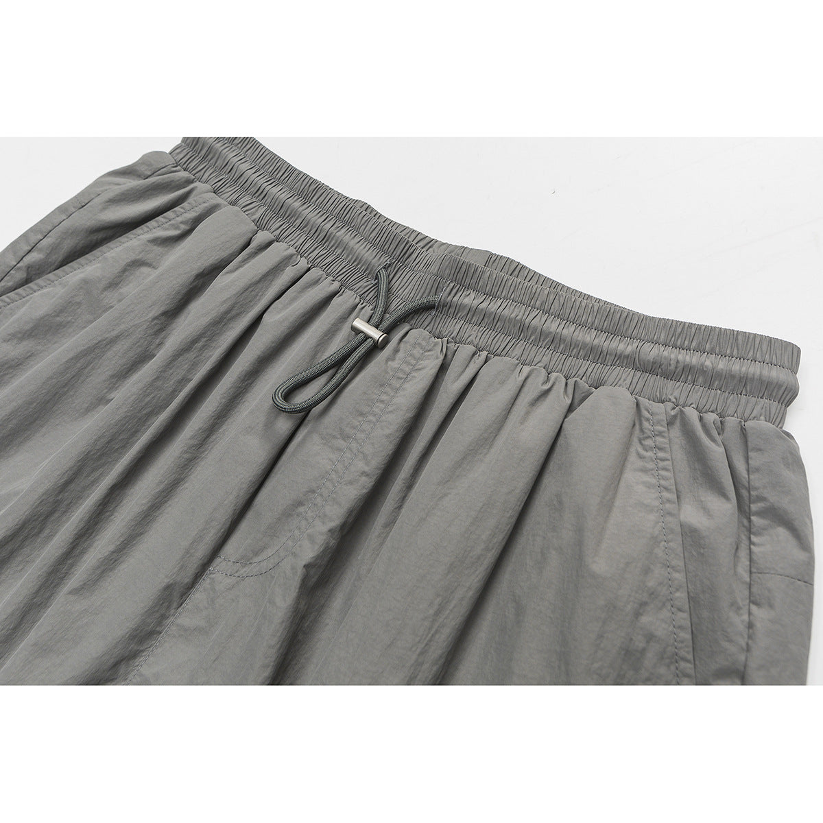 Close-up of gray shorts showing the gathered elastic waistband and dark drawcord with a metal tip.