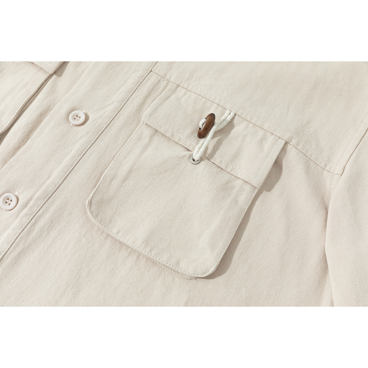 Close-up of a cream herringbone shirt's buttoned chest pocket with a wooden toggle and cord.