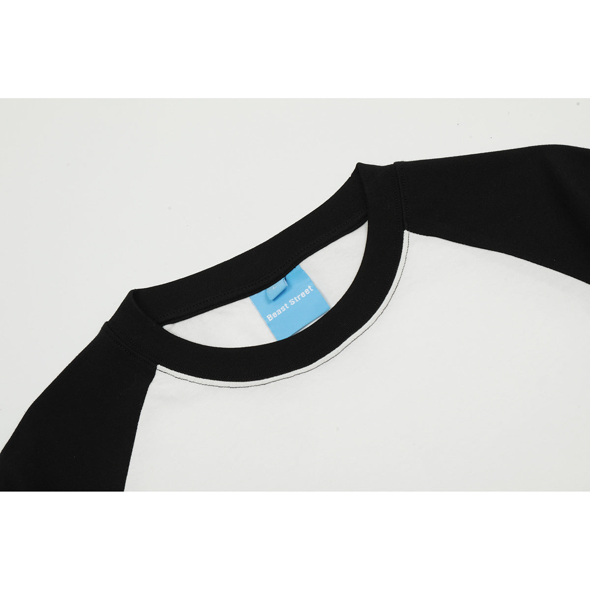 Close-up of a black ribbed crew neck and shoulder panels on a white raglan T-shirt, with a blue neck label.