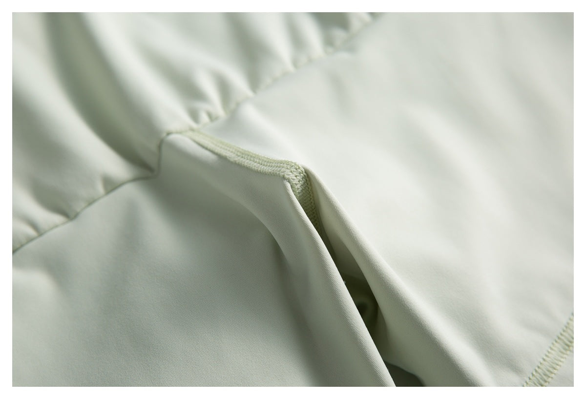 Close-up of pale mint fabric with gathered sections and a folded, overlocked seam.