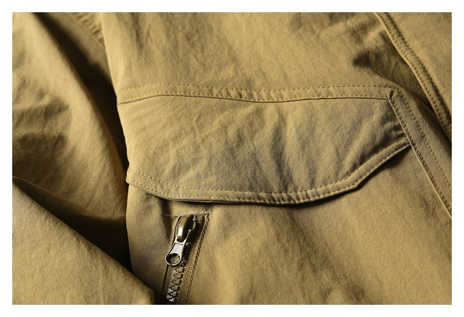 Close-up of a tan olive jacket with a curved flap pocket and zipper pocket beneath it.