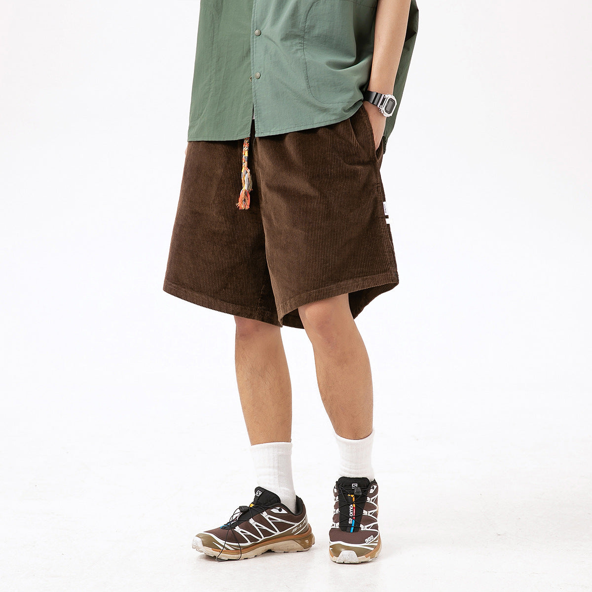 Model wearing brown knee-length shorts with a colorful braided tassel drawstring and side pockets.