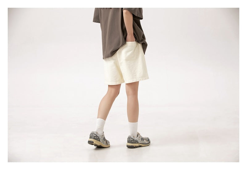 Rear three-quarter view of a model wearing cream loose shorts with a dark brown top.