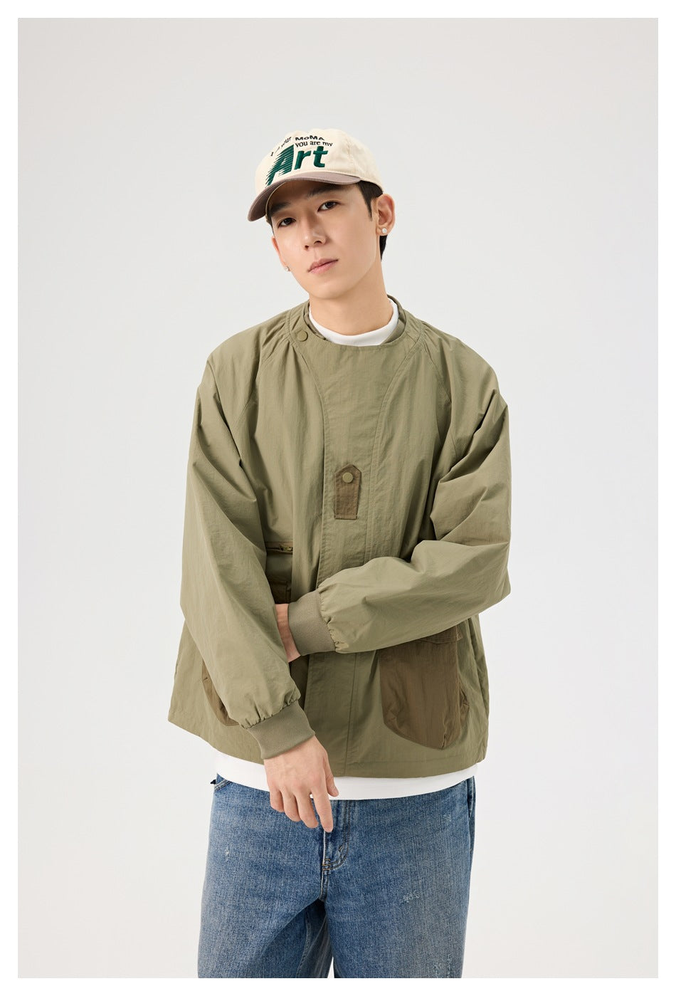 Model wearing an olive utility jacket with brown pockets, ribbed cuffs and a high snap collar, styled with jeans.