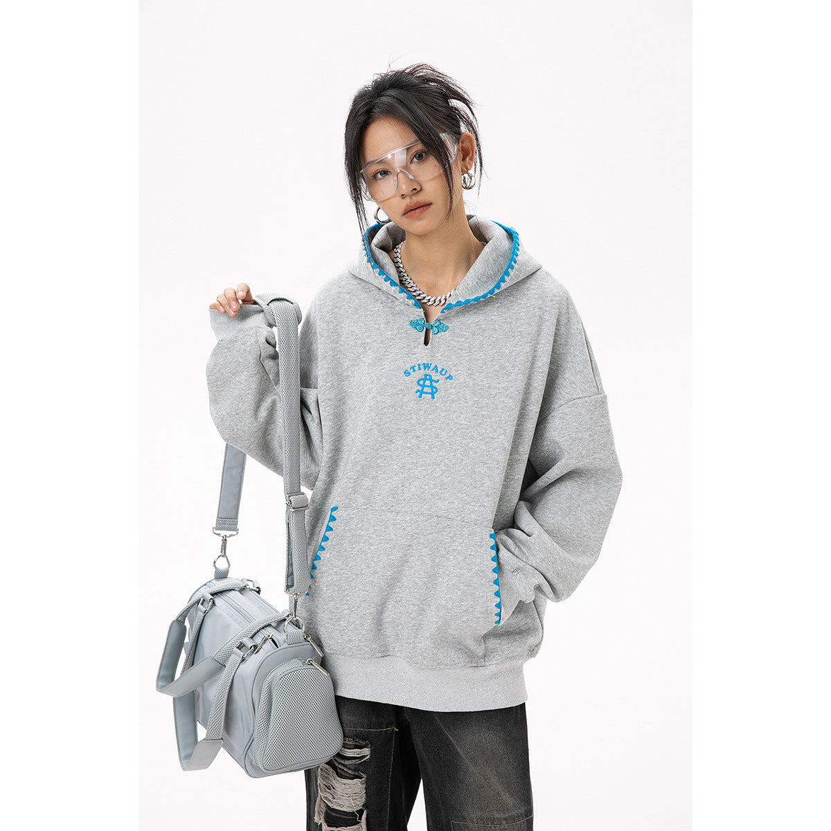 Model wearing an oversized gray hoodie with bright blue trim and kangaroo pocket, paired with black distressed jeans.