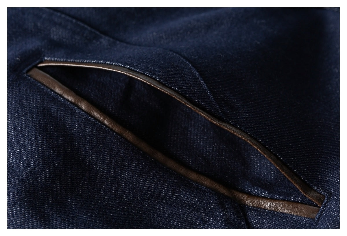 Close-up of a diagonal pocket opening edged with brown trim on the dark indigo jacket.
