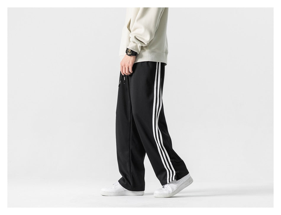 Cropped model in a side view wearing black track pants with three white stripes down the leg.