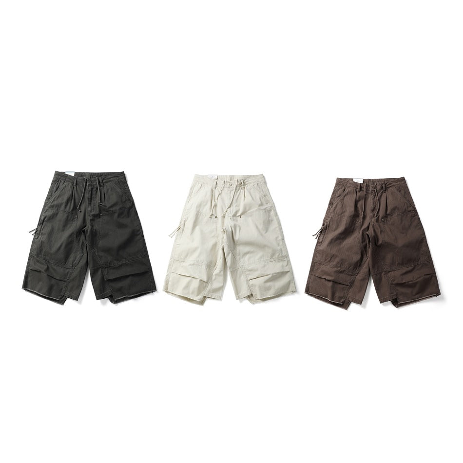 Three pairs of wide-leg utility shorts shown from the front in dark charcoal, cream and brown.