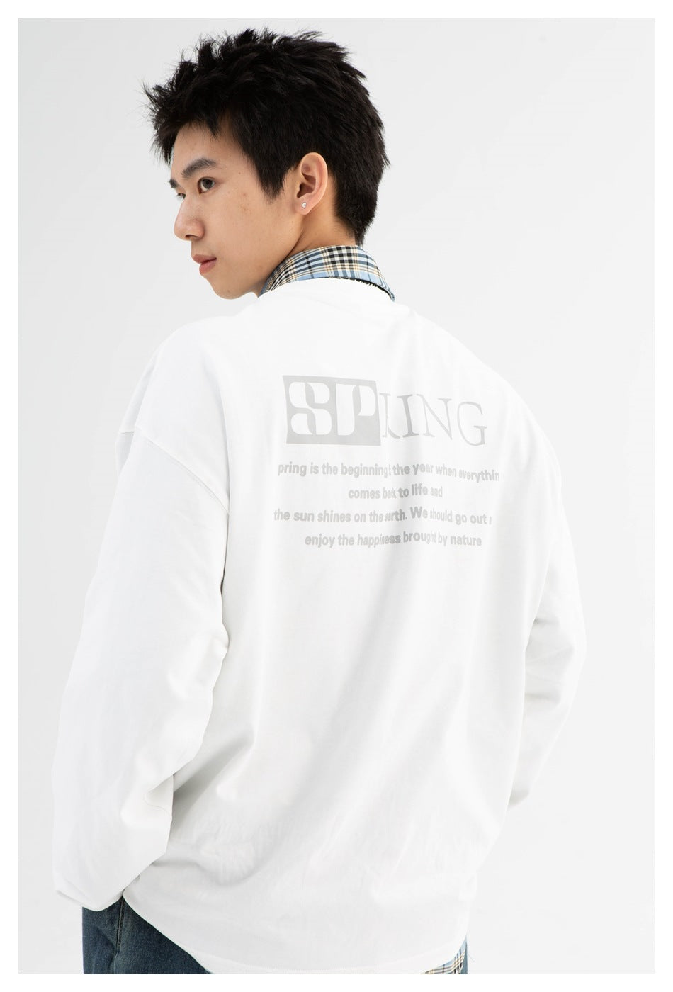 Rear view of a model wearing a white oversized long-sleeve top with pale gray SPRING text on the back.