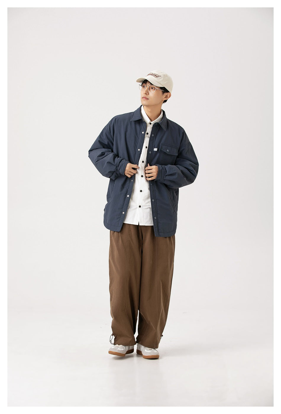 Model wearing a navy snap-front jacket over a white shirt with brown wide-leg pants, full-length view