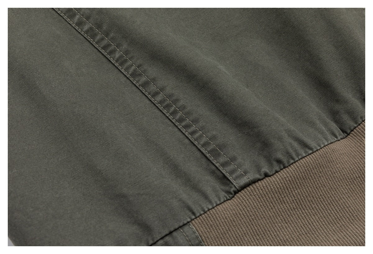 Close-up of olive-gray jacket fabric, stitched seams, and a taupe ribbed hem.