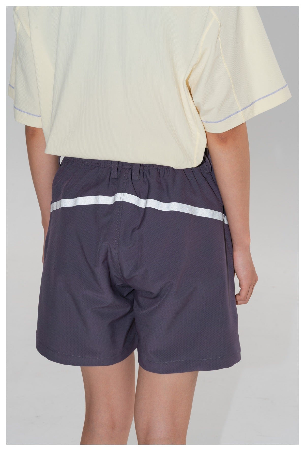Rear view of a model wearing dark purple shorts with a reflective band across the back.