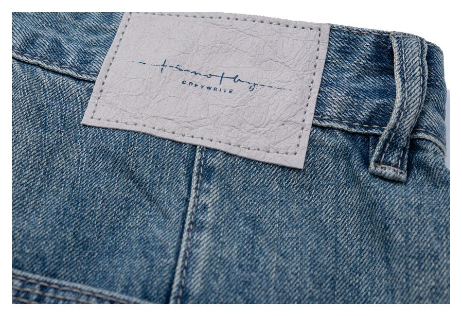 Close-up of blue denim jeans showing the waistband, belt loop, stitching, and a pale rectangular brand patch.
