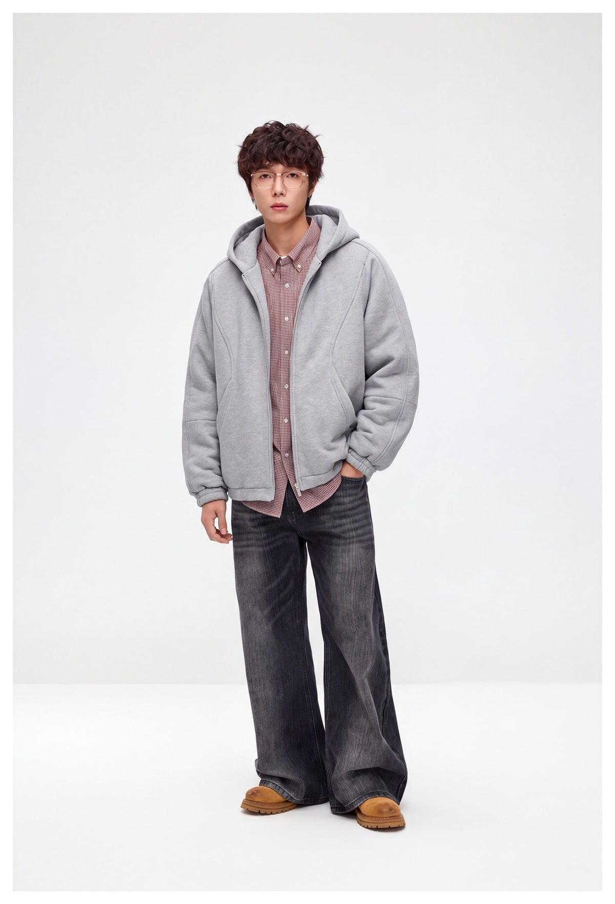 Model wearing open light gray hooded jacket over a red checked shirt with wide dark jeans and tan boots