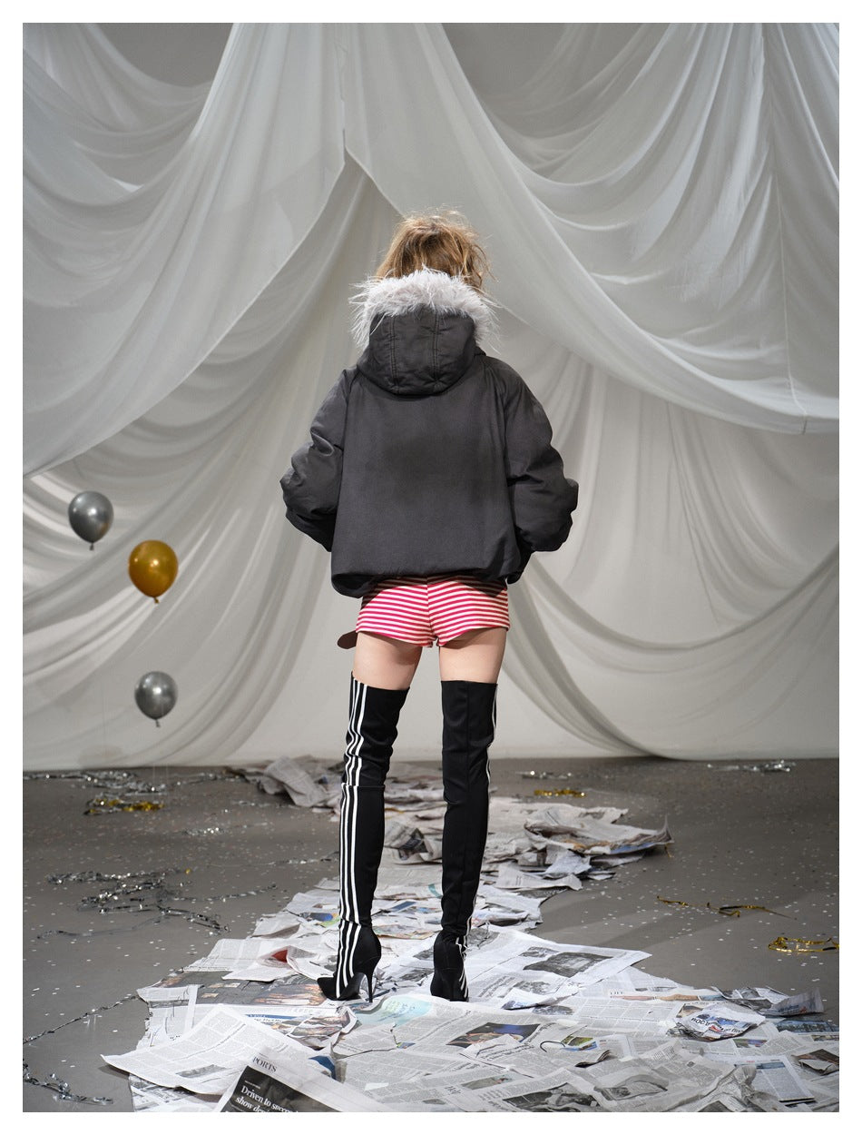 Rear view of a model wearing a dark hooded jacket with pale fur trim, red-and-white striped shorts and black thigh-high