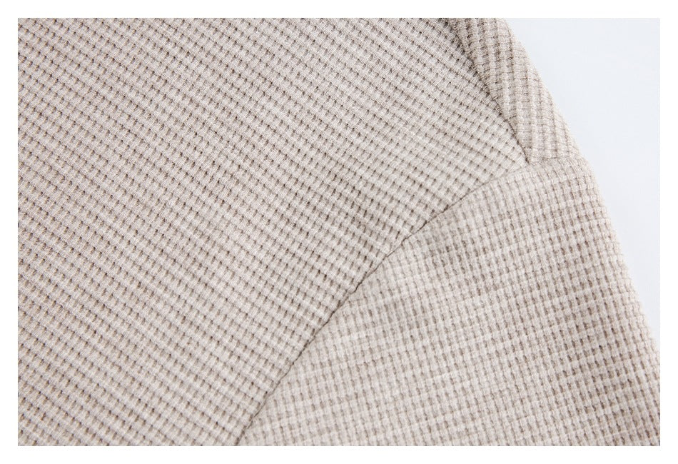 Close-up of the beige textured top's fabric and curved sleeve seam against a white background.