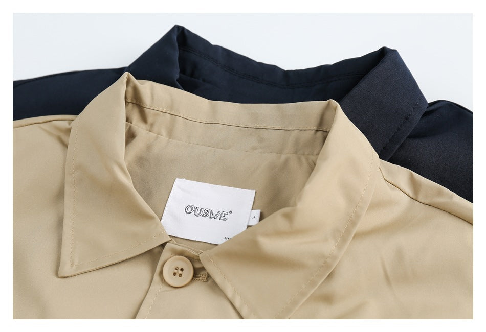 Close-up of a beige coat collar and button with a sewn OUSWE label; a dark coat is visible behind it.