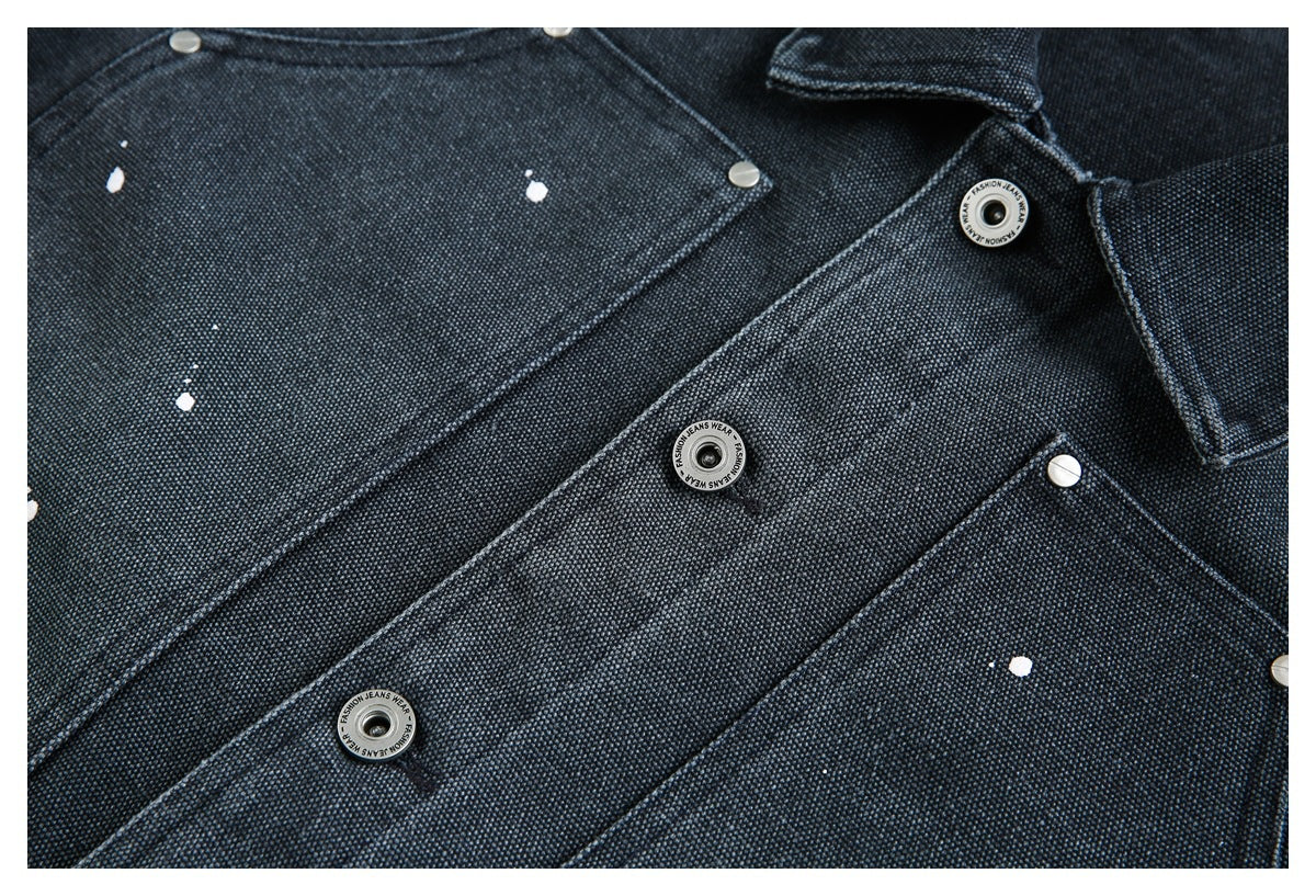 Close-up of a dark indigo jacket front with silver snaps, flap pockets, and scattered white paint-like marks.
