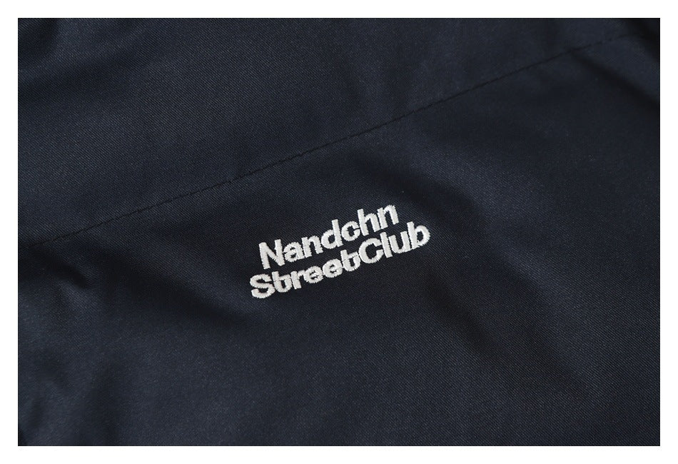 Close-up of white embroidered lettering on the dark navy jacket chest.