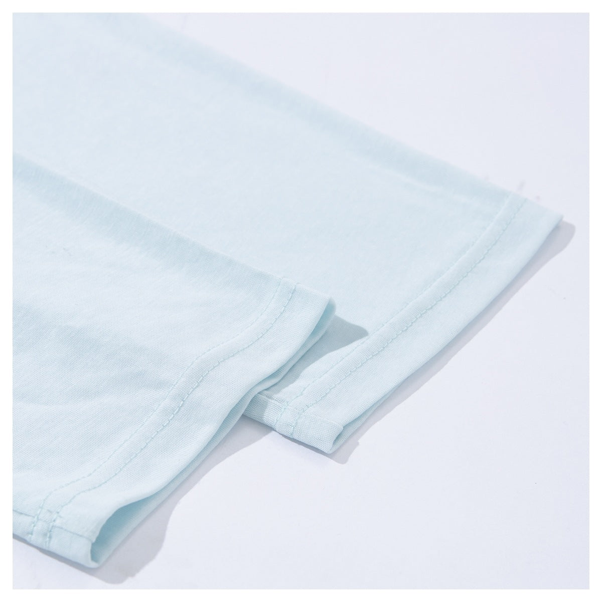 Close-up of overlapping stitched edges on a pale blue T-shirt laid flat.