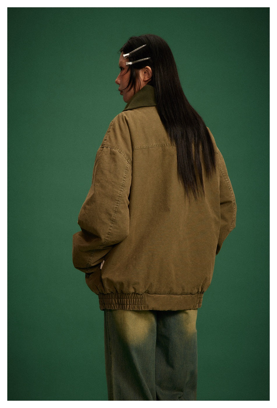 Back view of a model in an oversized olive-brown jacket with a dark collar and gathered hem.