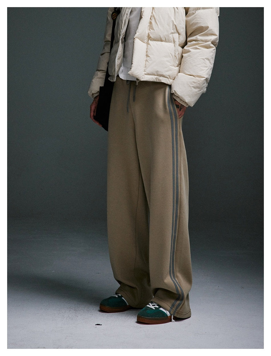 Person wearing khaki wide-leg sweatpants with gray side stripes, cropped below the chest, with green sneakers