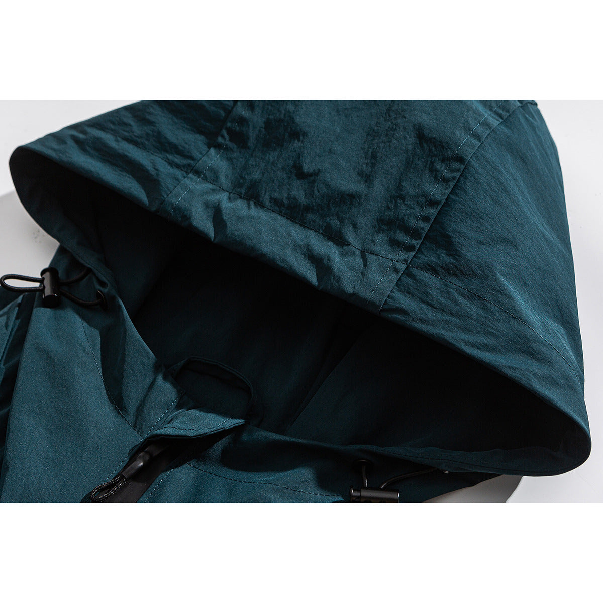 Close-up of a deep teal jacket hood with black lining and adjustable drawcords.