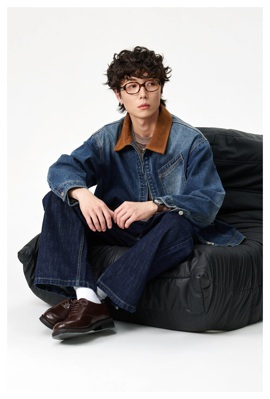 Seated model wearing a medium-wash denim jacket with a brown collar and chest pocket.