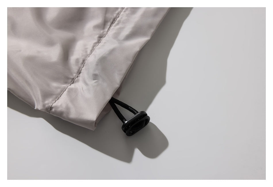 Close-up of a light taupe jacket hem with a black drawcord toggle.