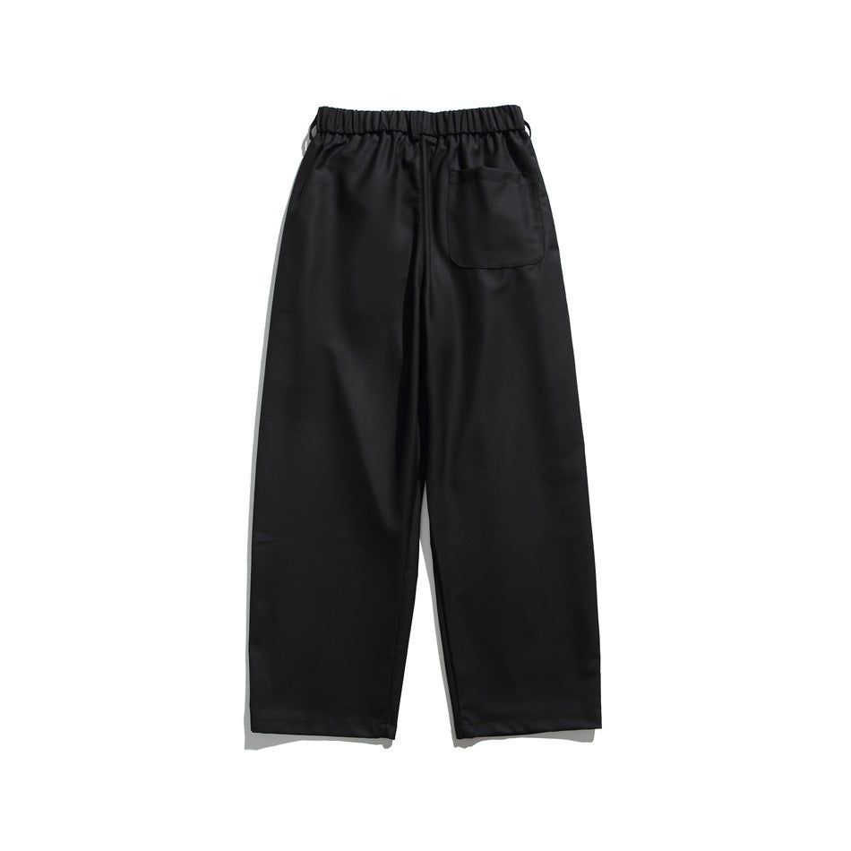 Black wide-leg trousers back view with elastic waistband and a single patch pocket, flat lay