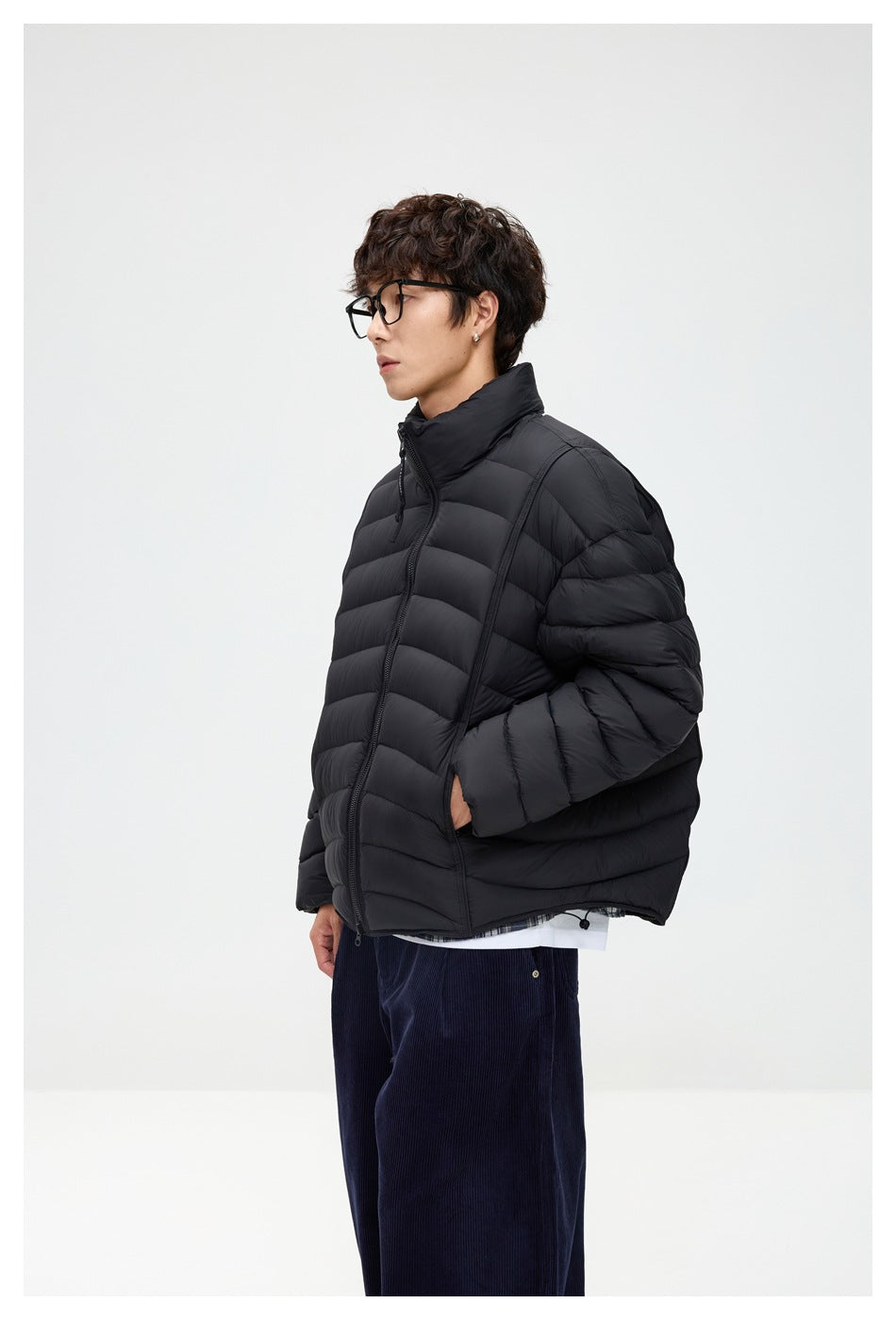 Side view of a model wearing a black quilted puffer jacket with a high collar and front zipper.