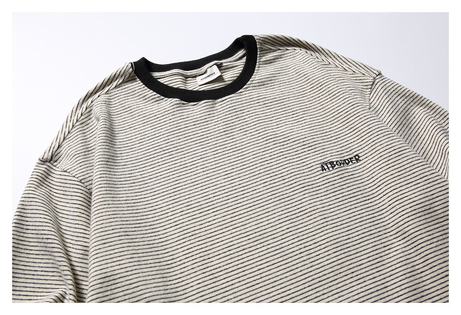 Close view of an off-white striped shirt front with black crew neck and small dark embroidered chest lettering.