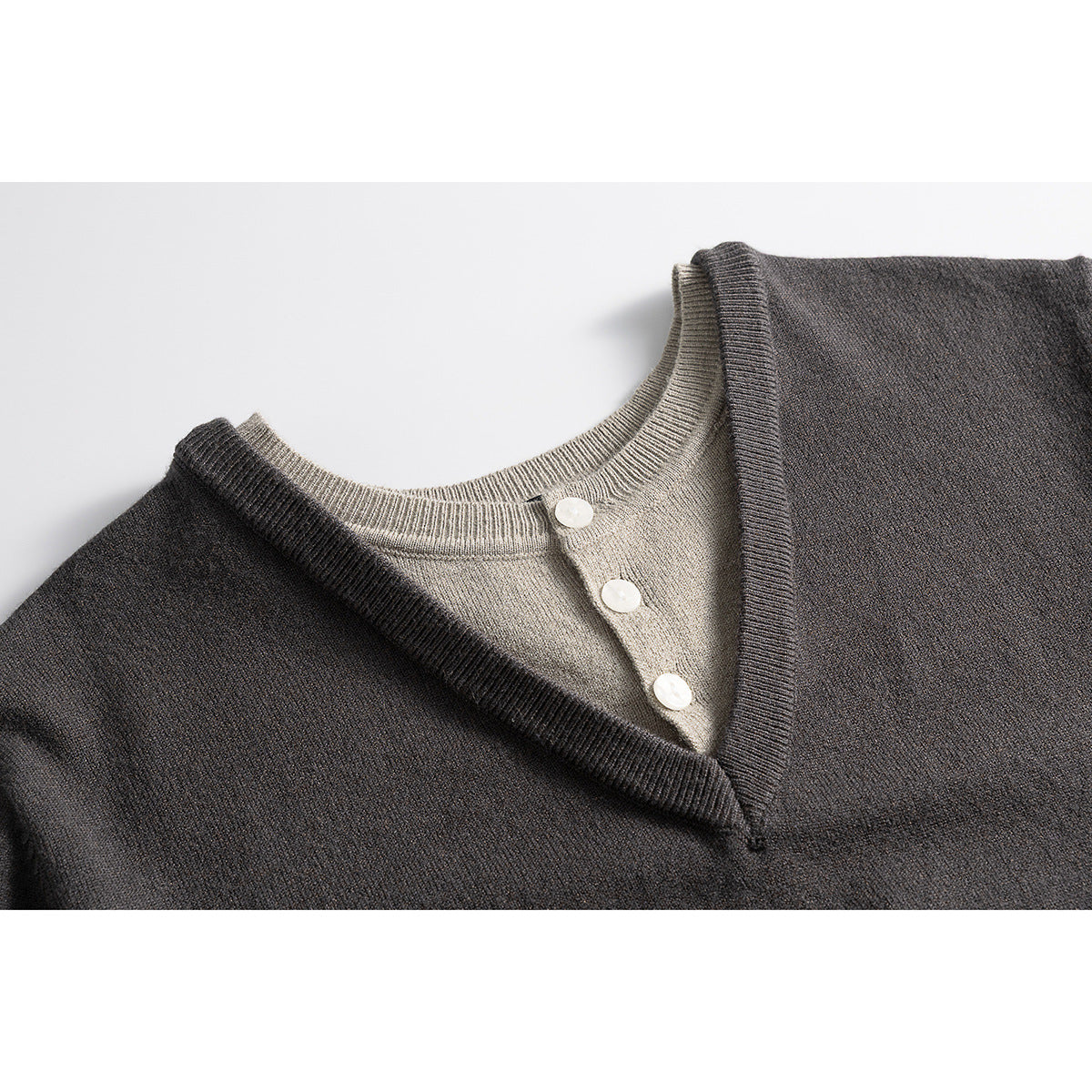 Close-up of a charcoal V-neck sweater layered over a light beige button-front knit neckline.