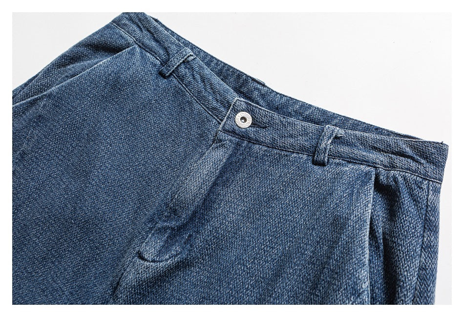 Close-up of dark blue denim trousers showing the waistband, belt loops, metal button and fly seam.