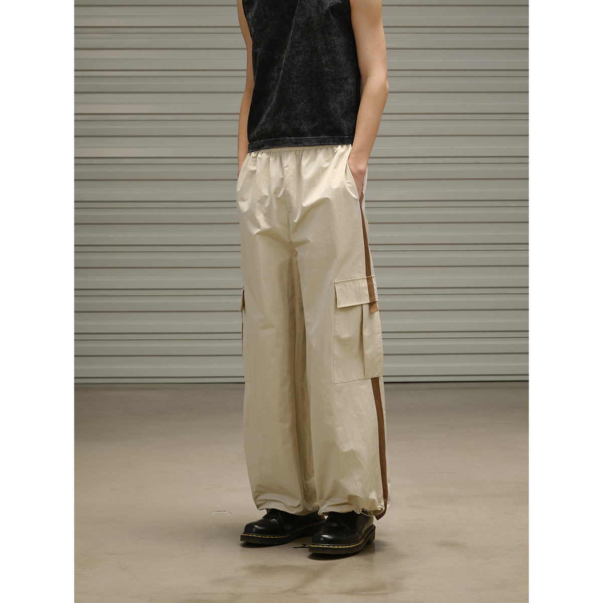 Cropped view of a model wearing loose beige cargo pants with large side pockets and a black sleeveless top.
