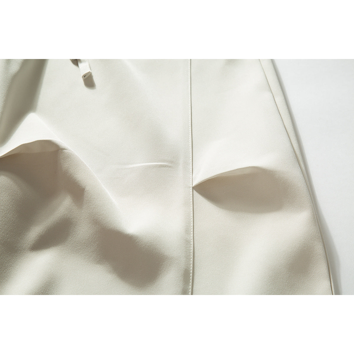 Close-up of cream trousers showing a vertical seam, smooth fabric, and a partial drawstring.