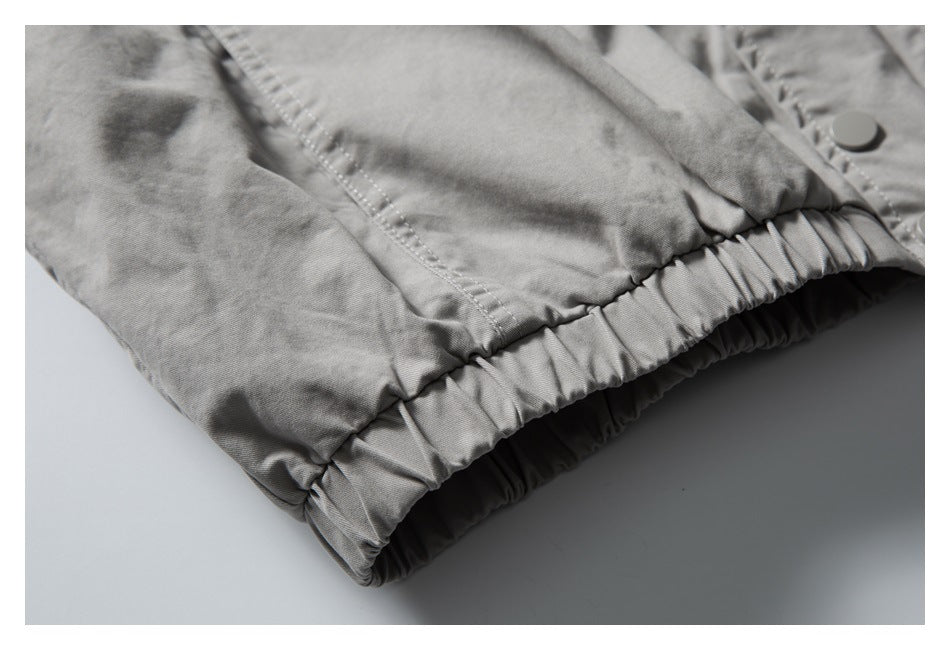 Close-up of a gathered elastic hem and snap button on a light gray garment.