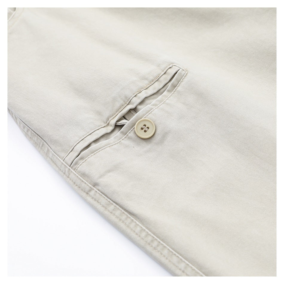 Close-up of light beige pants showing a small buttoned pocket opening and stitched seams.