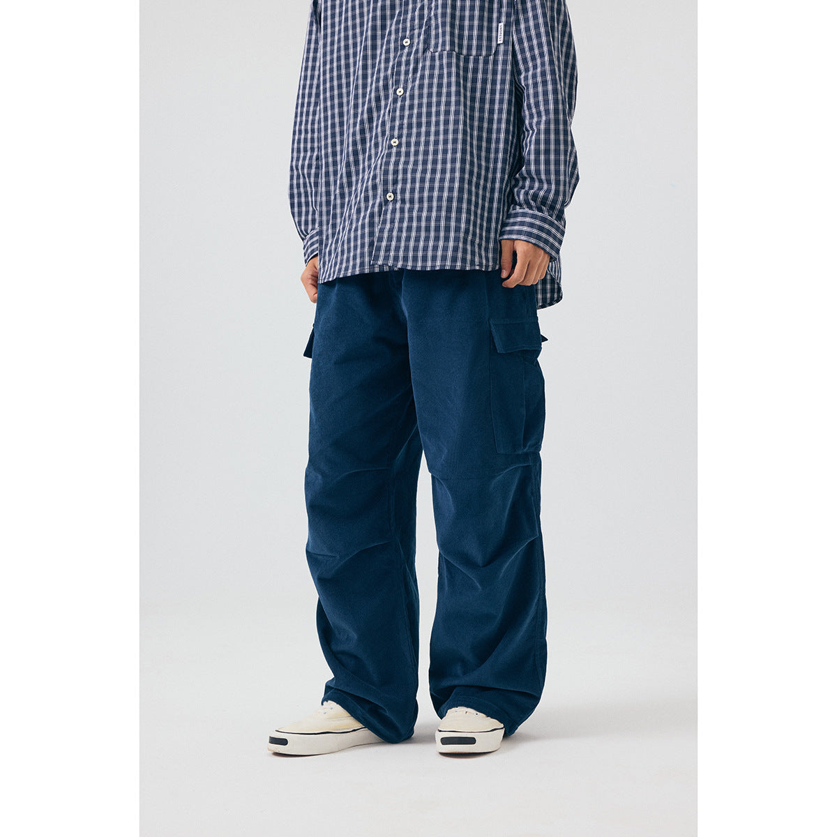 Front view of a model wearing loose navy cargo pants with large thigh pockets and a blue-and-white check shirt.