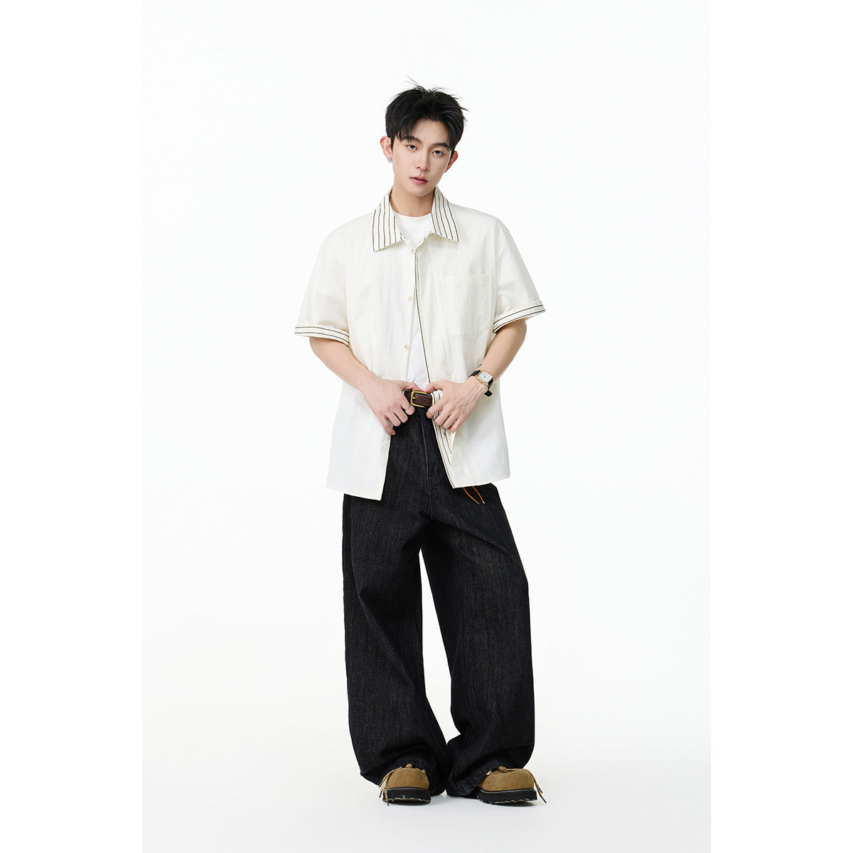 Model wearing an oversized ivory short-sleeve shirt with striped collar and cuff trim, paired with wide black jeans.