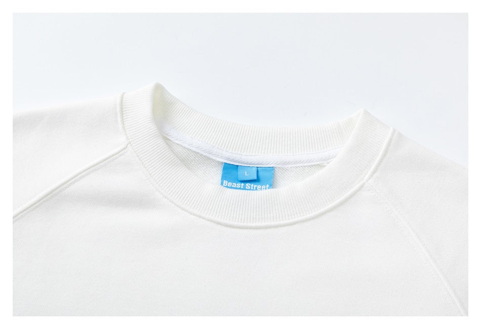 Close-up of a white sweatshirt's ribbed crew neckline, raglan seams, and blue size and brand label.