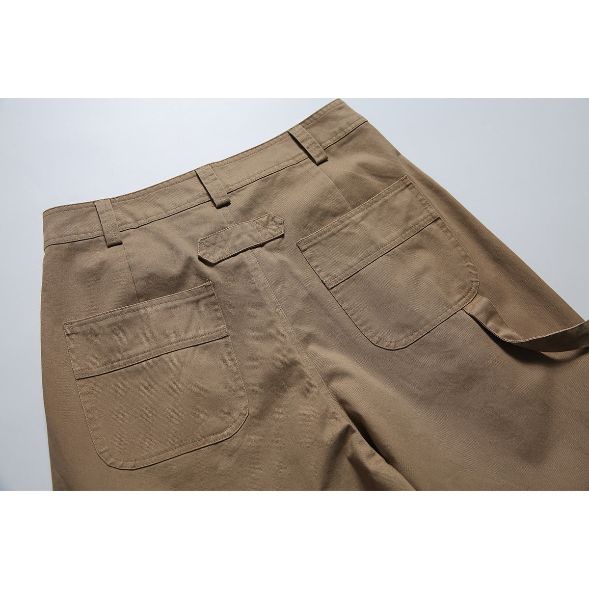 Close-up of the back of brown trousers, showing two patch pockets, belt loops, and a center tab.