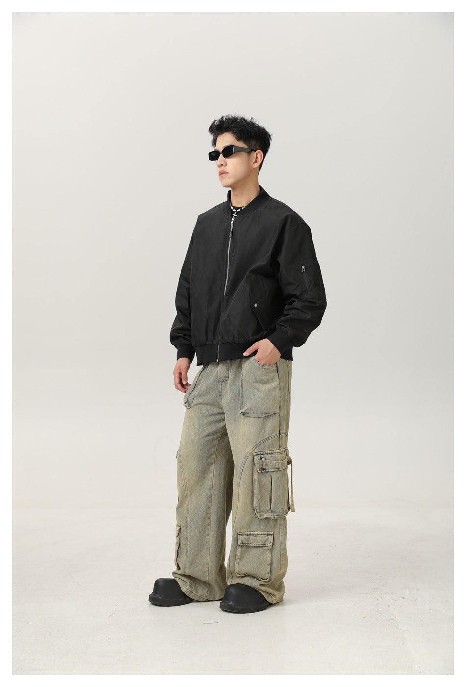 Model wearing a black bomber jacket with a zippered sleeve pocket and snap-front side pockets.