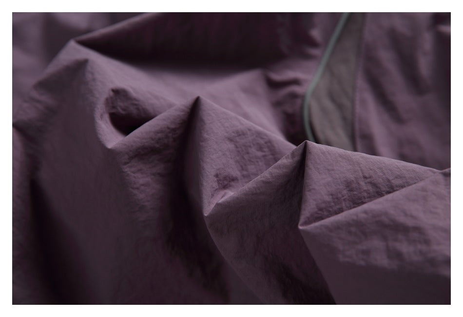 Macro view of the plum garment's crinkled fabric and gray-piped seam.
