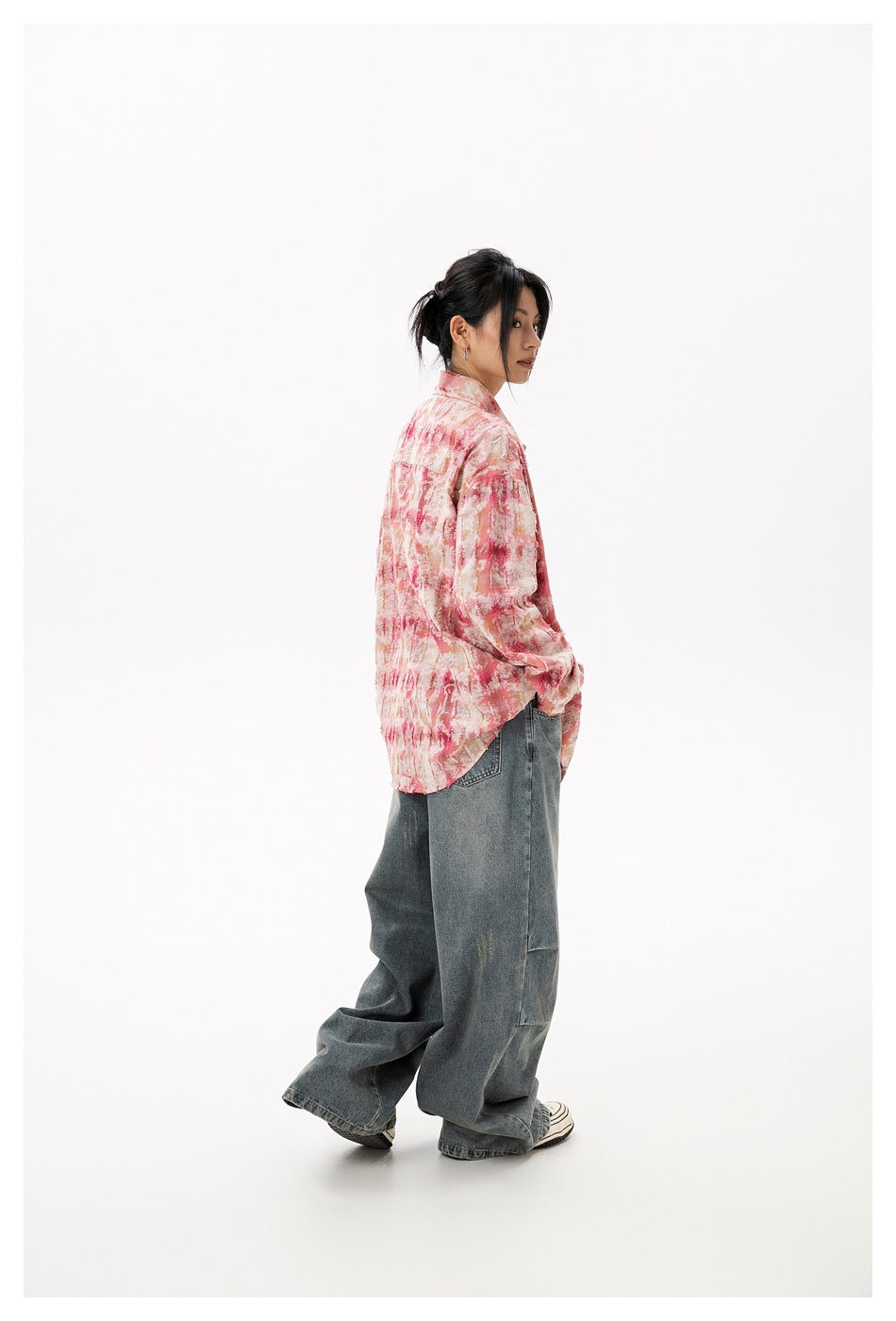 Model in pink tie-dye plaid shirt and wide-leg faded jeans, side view looking back over her shoulder