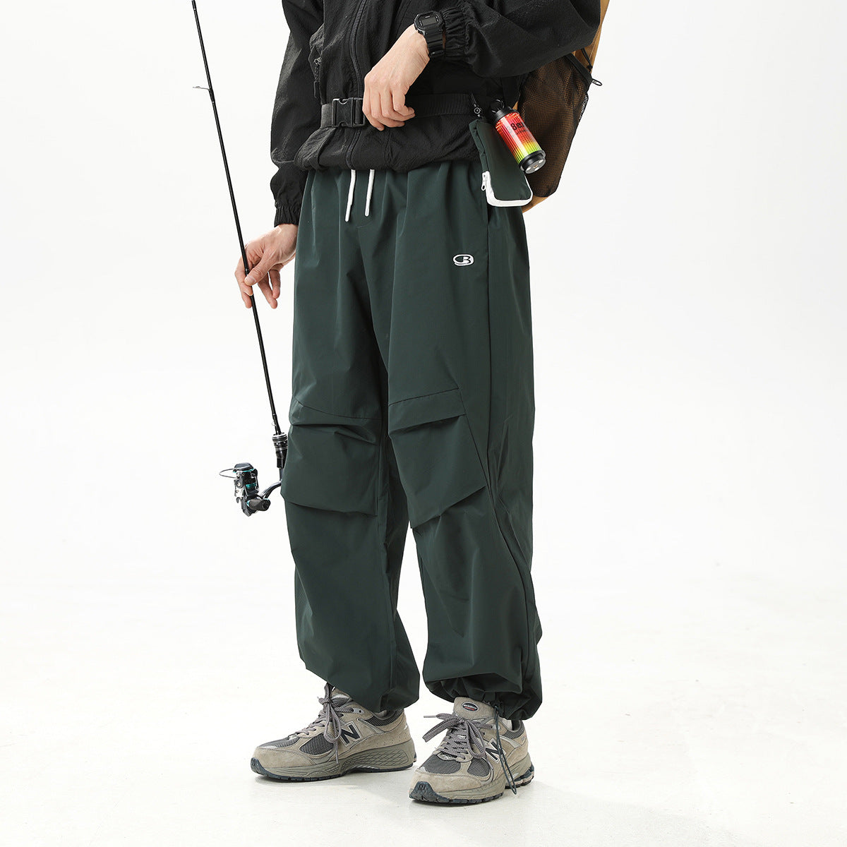 Cropped model wearing dark forest-green, loose cargo pants with large layered pockets and drawstring waist.